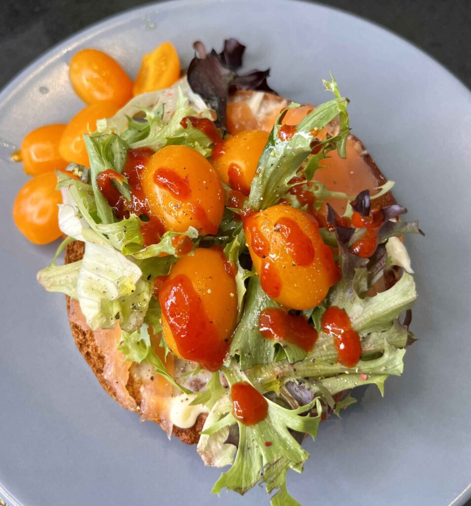 Smoked salmon, a perfectly baked egg, and cream cheese on a toasted bagel, topped with fresh salad and cherry tomatoes