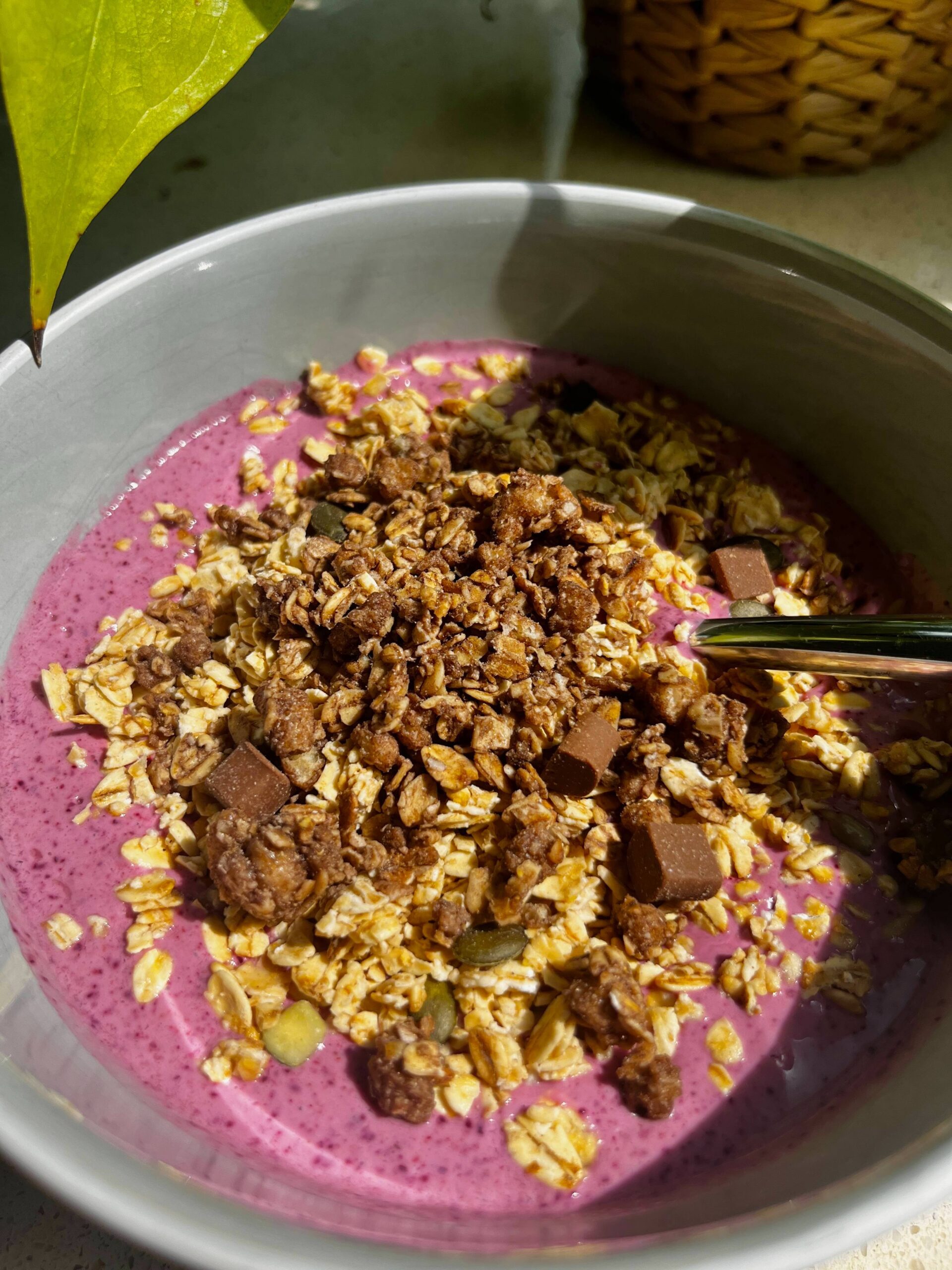 Nutritious mixed berry smoothie bowl topped with granola, oats, pumpkin seeds, and chocolate chunks, served in a ceramic bowl under natural sunlight — ideal healthy breakfast or post-workout meal option.